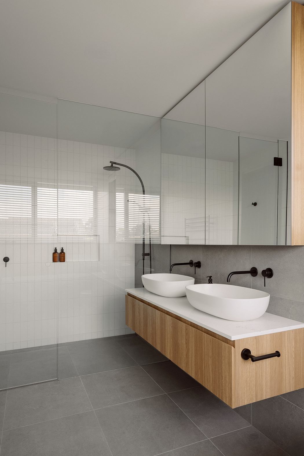 Minimalist bathroom with wooden vanity, vessel sinks, and black fixtures against tiled walls.