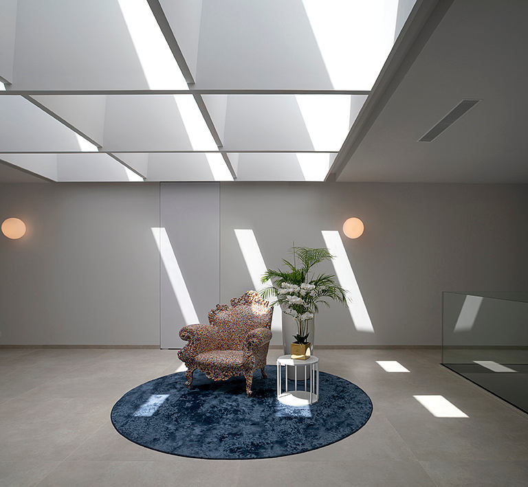 Spacious, modern interior with geometric lighting, plush armchair, and potted plant.