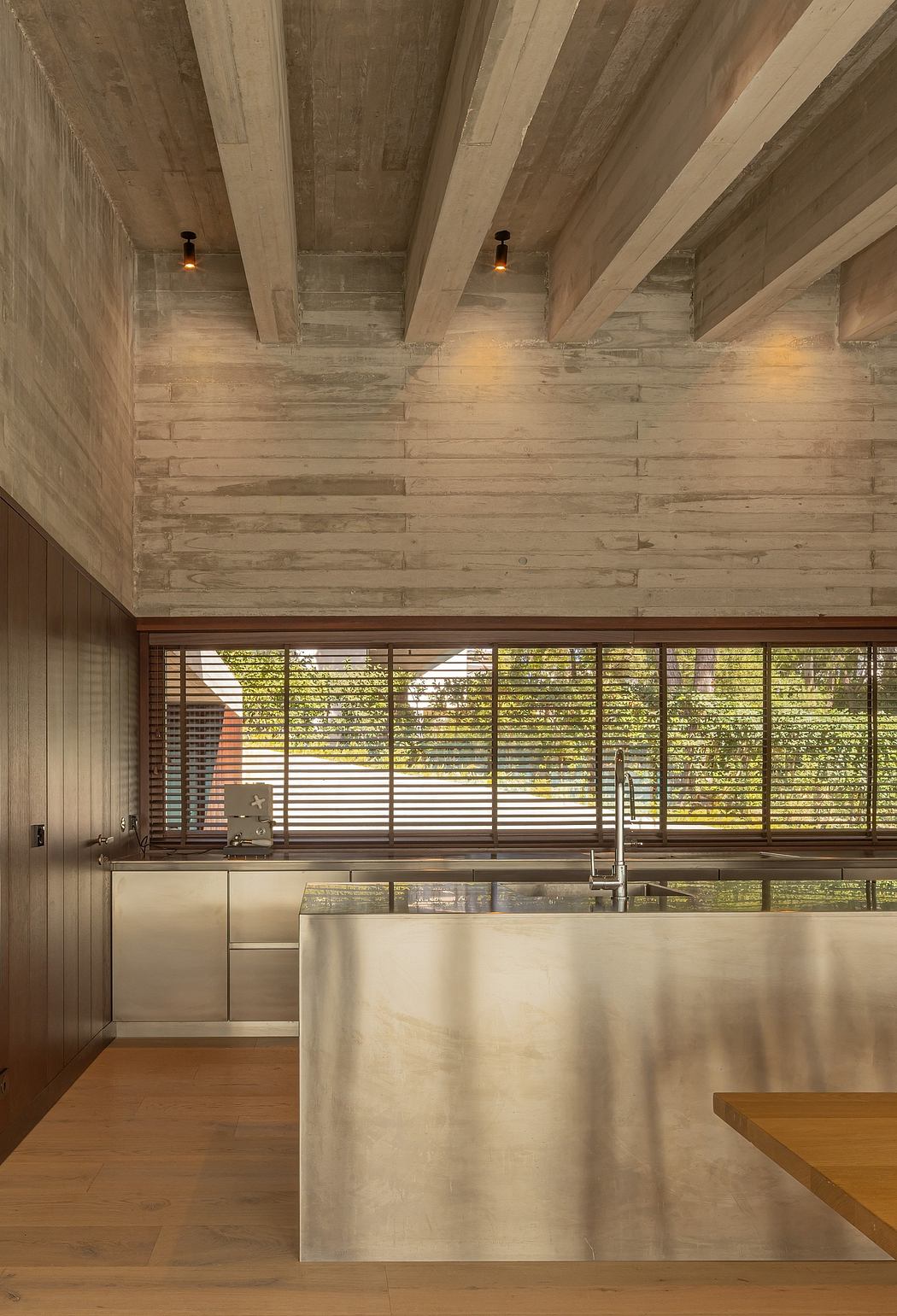 Rustic wooden ceiling, concrete walls, and large windows overlooking lush greenery.