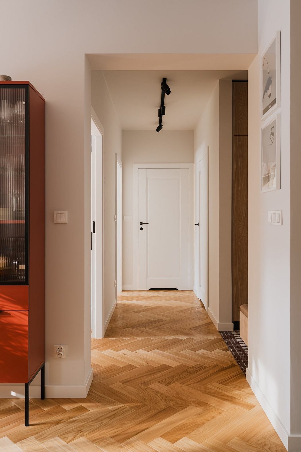 Bright, minimalist hallway with white walls, wood herringbone flooring, and modern lighting.