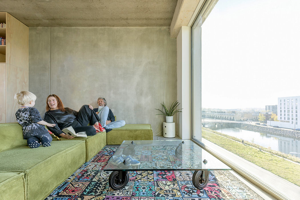 A modern, open-plan living space with concrete walls, a colorful patterned rug, and a large window overlooking the city.