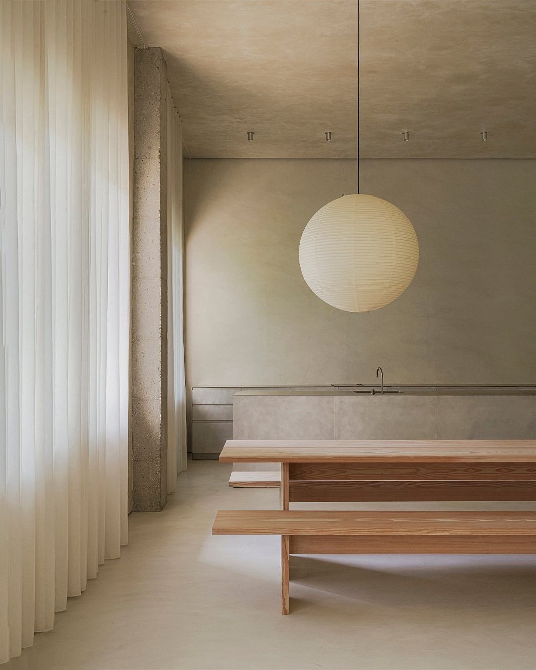 Minimalist interior with a spherical pendant lamp and a wooden dining table with benches.