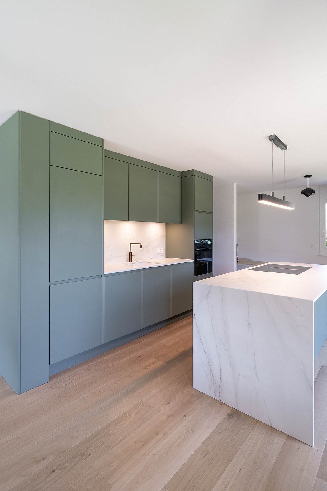 Sleek green cabinetry, marble countertop, and oak flooring create a modern, minimalist kitchen.