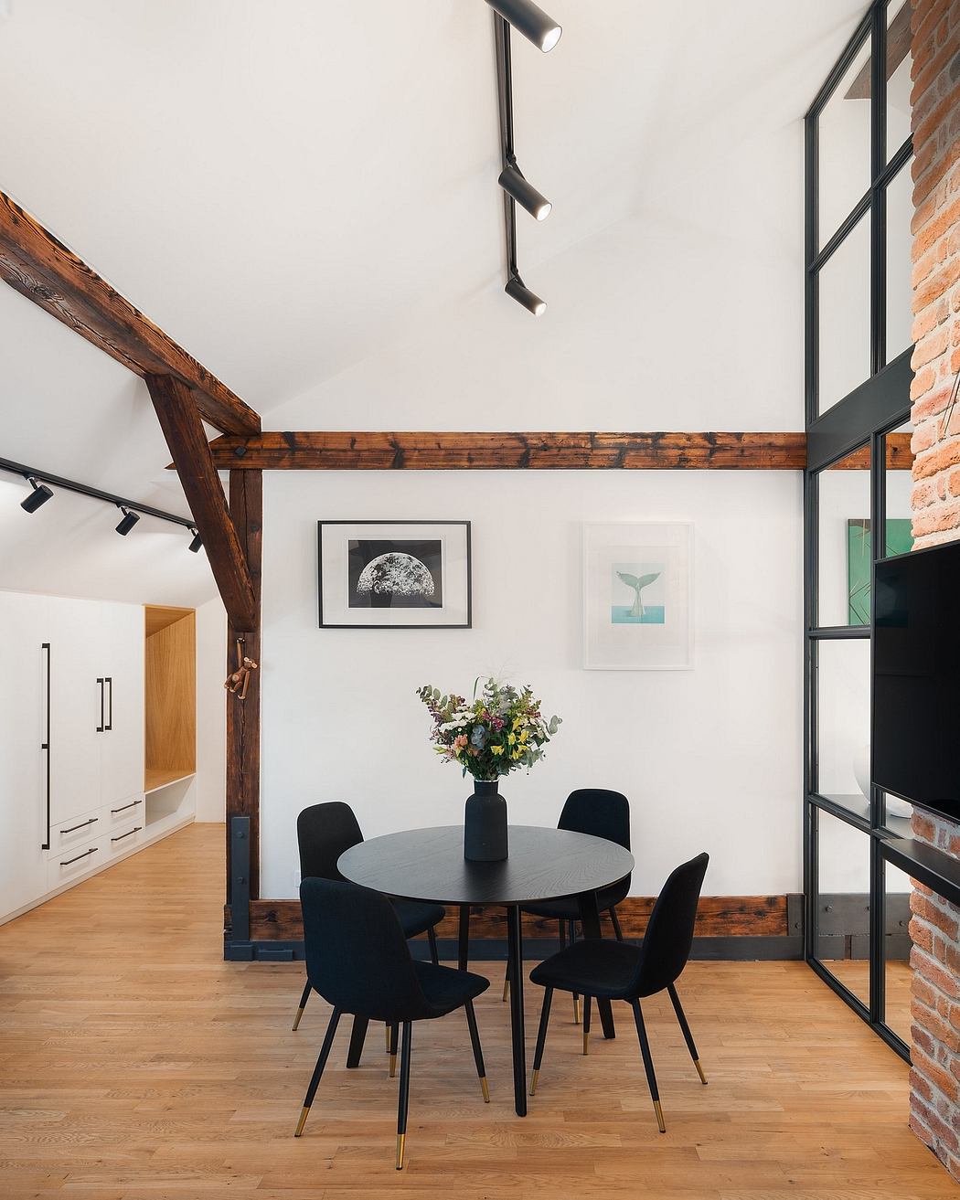 Bright, modern dining space with exposed wooden beams, black furniture, and artwork.