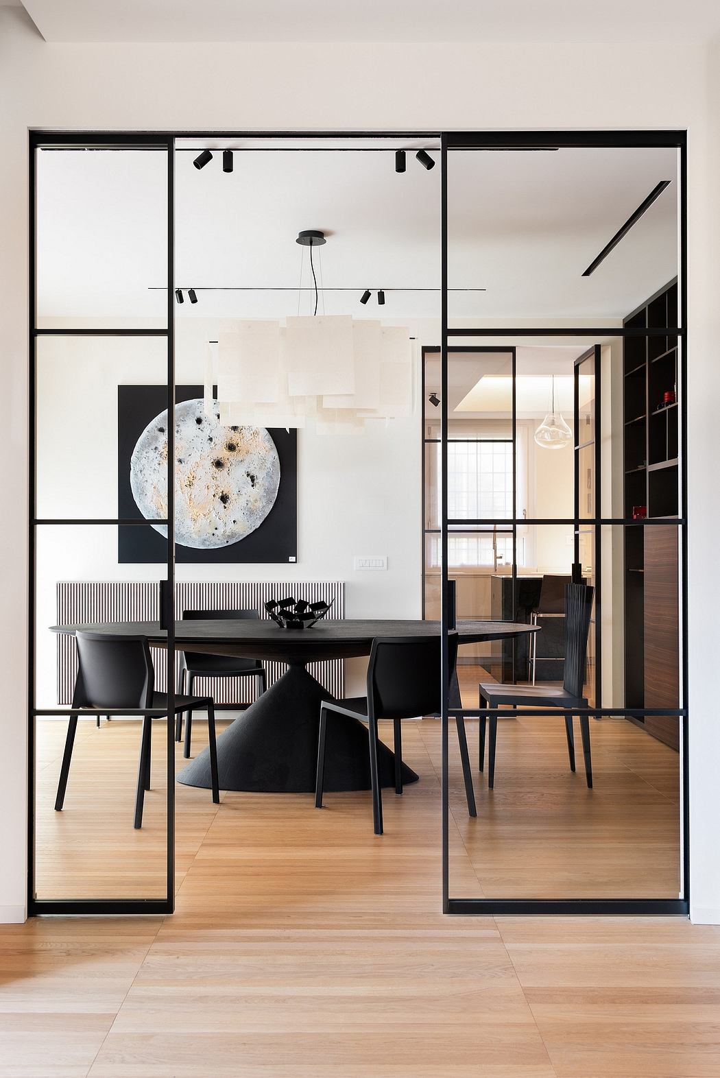 Minimalist dining room with sleek black-framed glass walls, modern furnishings, and artistic decor.