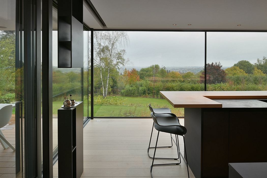 Sleek modern kitchen overlooking lush green landscape through vast glass walls.