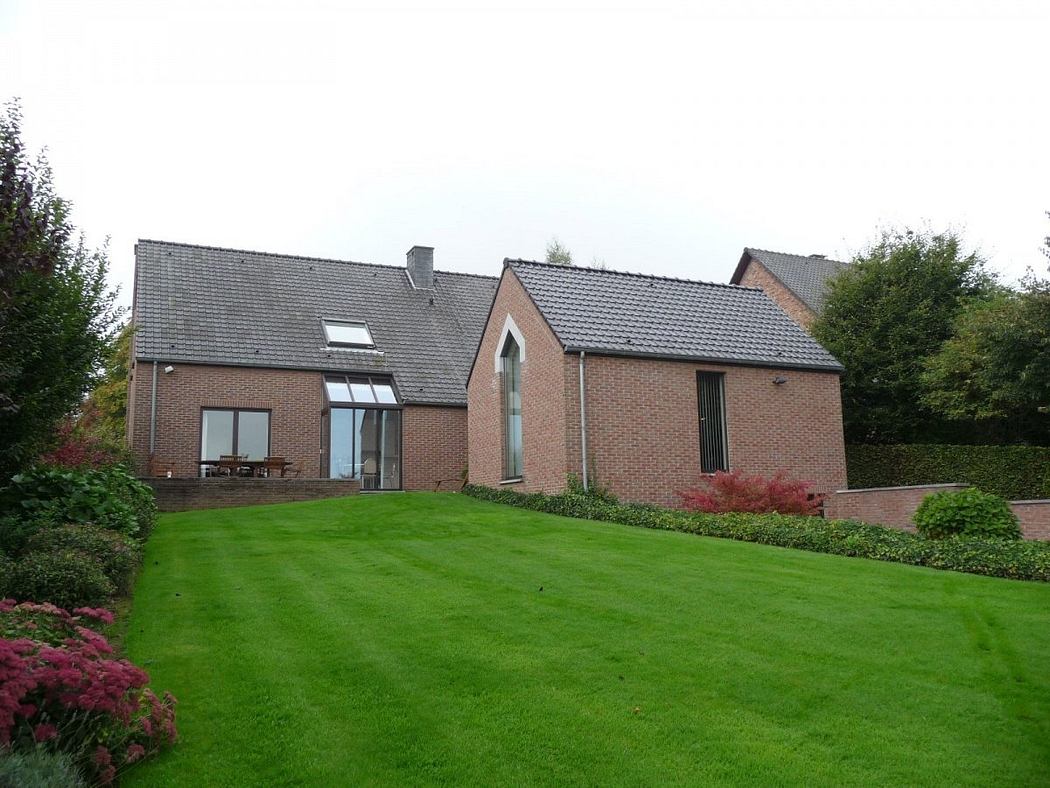 A modern brick house with a slanted roof, large windows, and a well-manicured lawn.