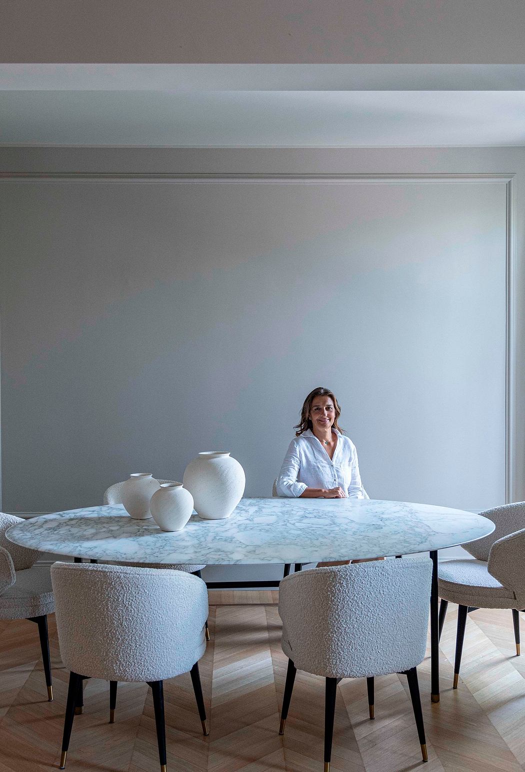 Elegant marble-topped dining table, plush upholstered chairs, and decorative pottery in minimalist space.