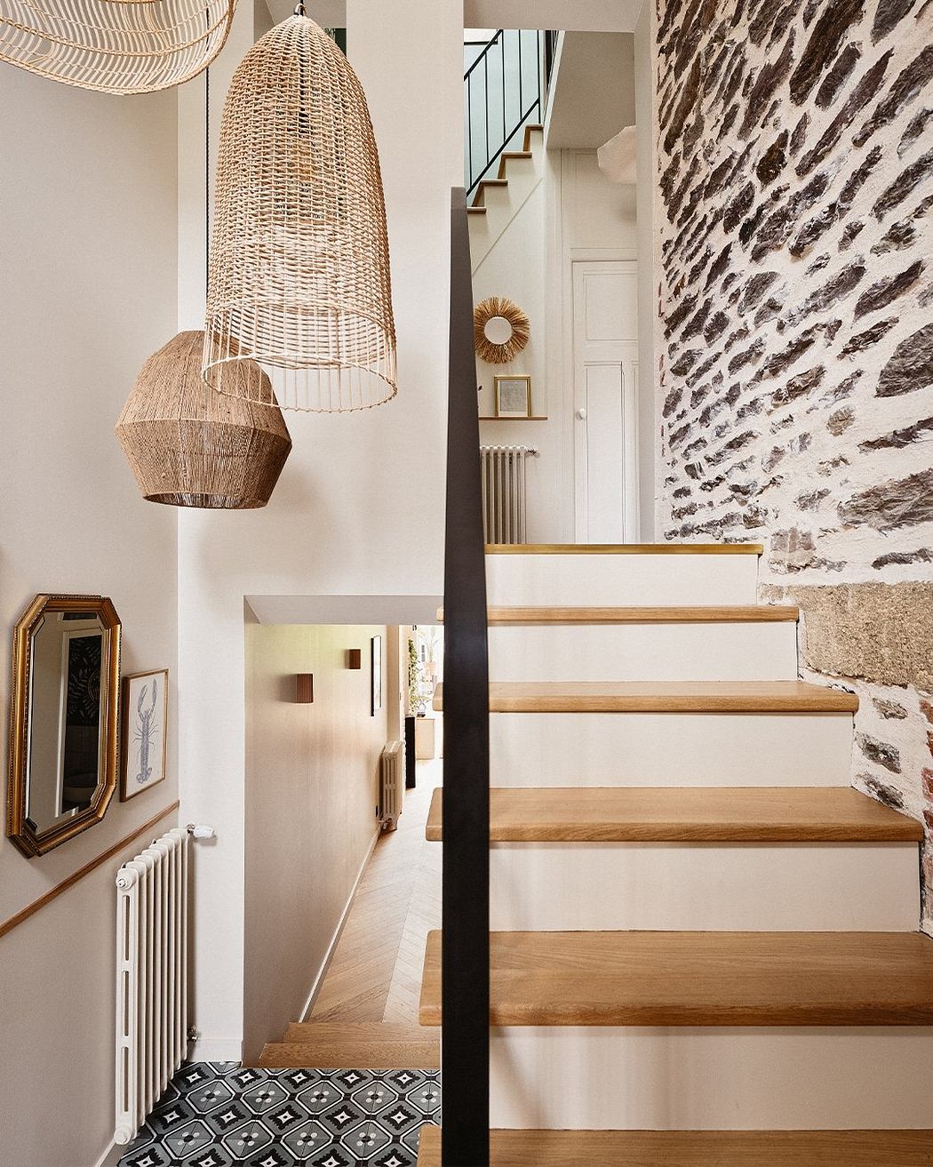 An inviting entryway with textured stone walls, wooden staircase, and modern pendant lamps.