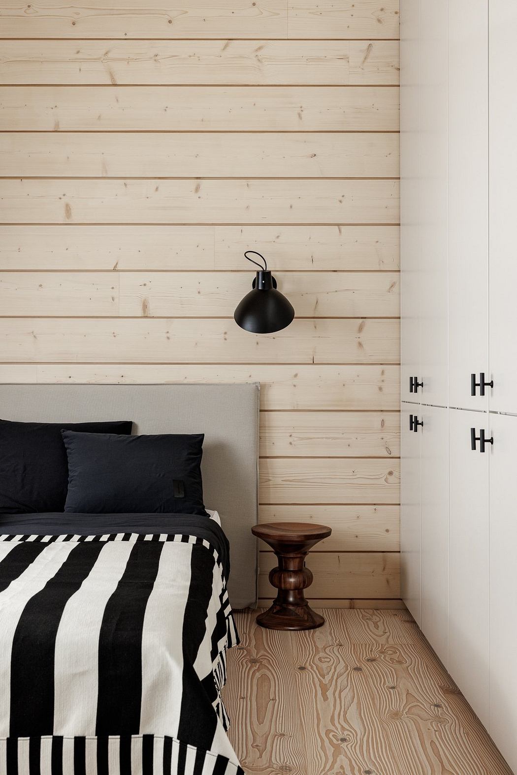 A cozy bedroom with wooden paneled walls, a black lamp, and a wooden stool by the bed.