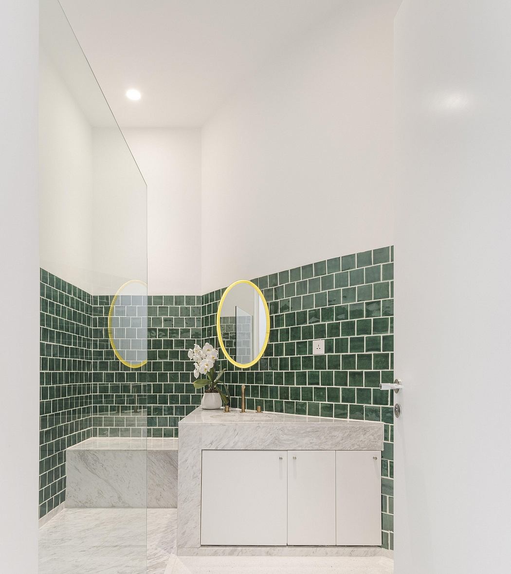 Modern bathroom with green mosaic tile walls, marble vanity, and circular mirrors.