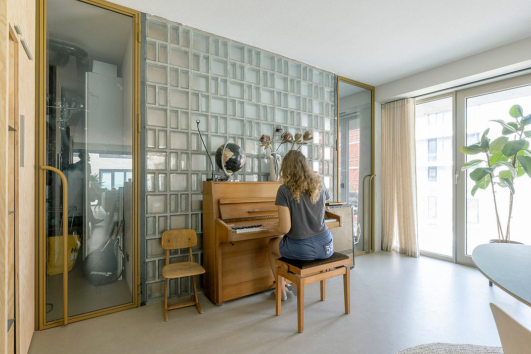 A modern room with a glass brick wall and a person playing an upright piano.