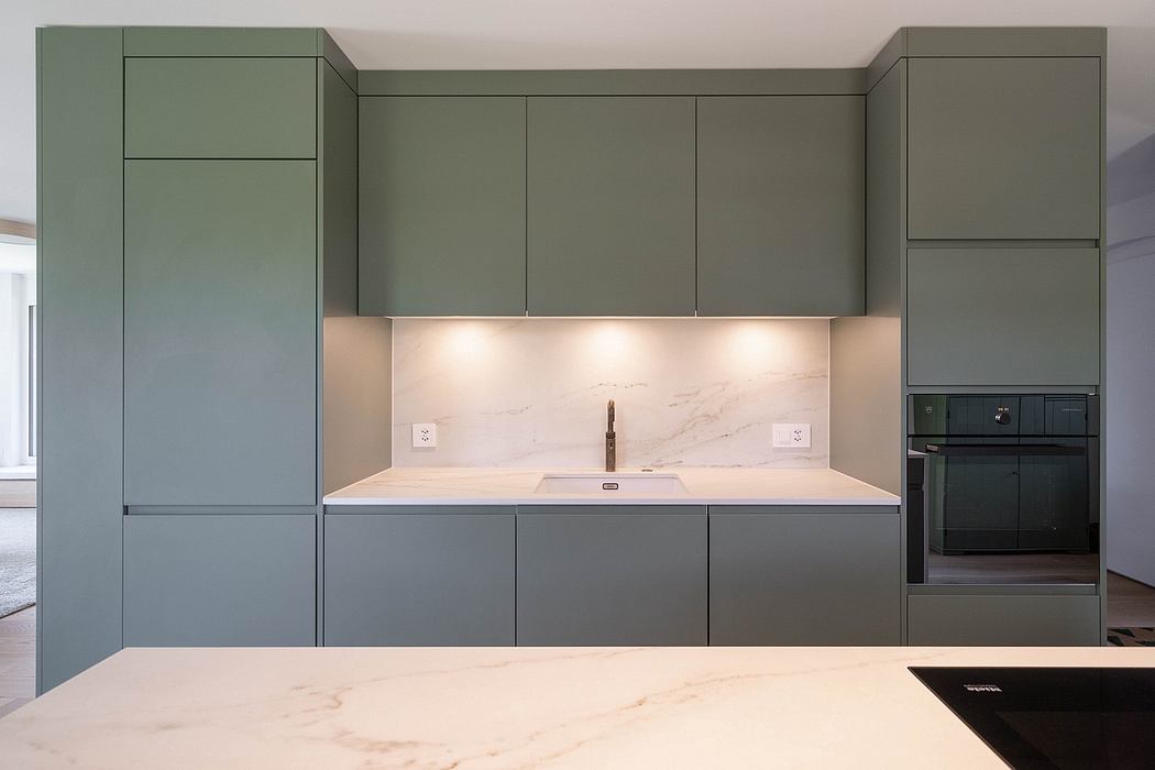 A modern kitchen with minimalist green cabinetry, sleek marble countertops, and recessed lighting.