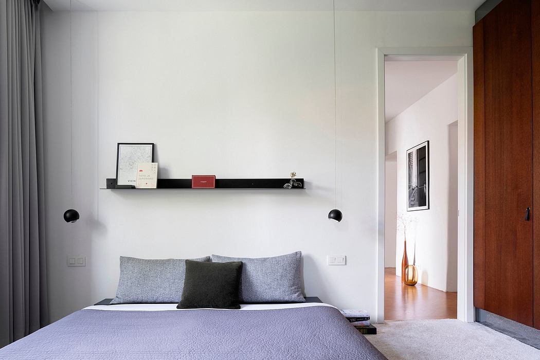 Minimalist bedroom with a sleek, modern design featuring a wooden doorway, gray bedding, and a floating shelf.