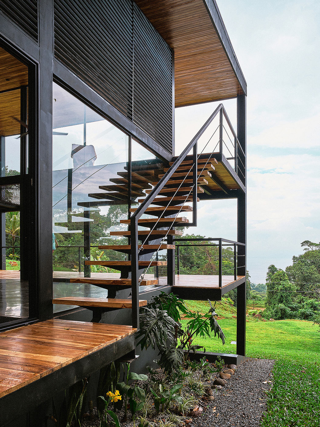 Modern architectural design with sleek steel frame, wood steps, lush greenery.