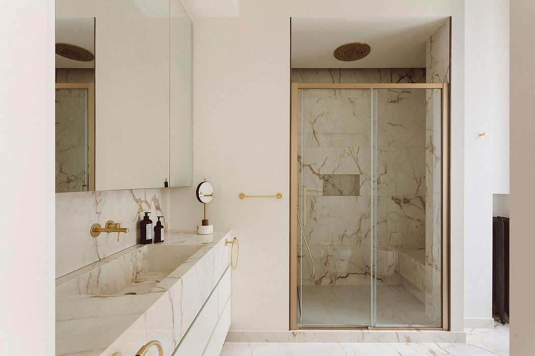 Spacious marble-clad bathroom with minimalist vanity, brass fixtures, and glass shower.