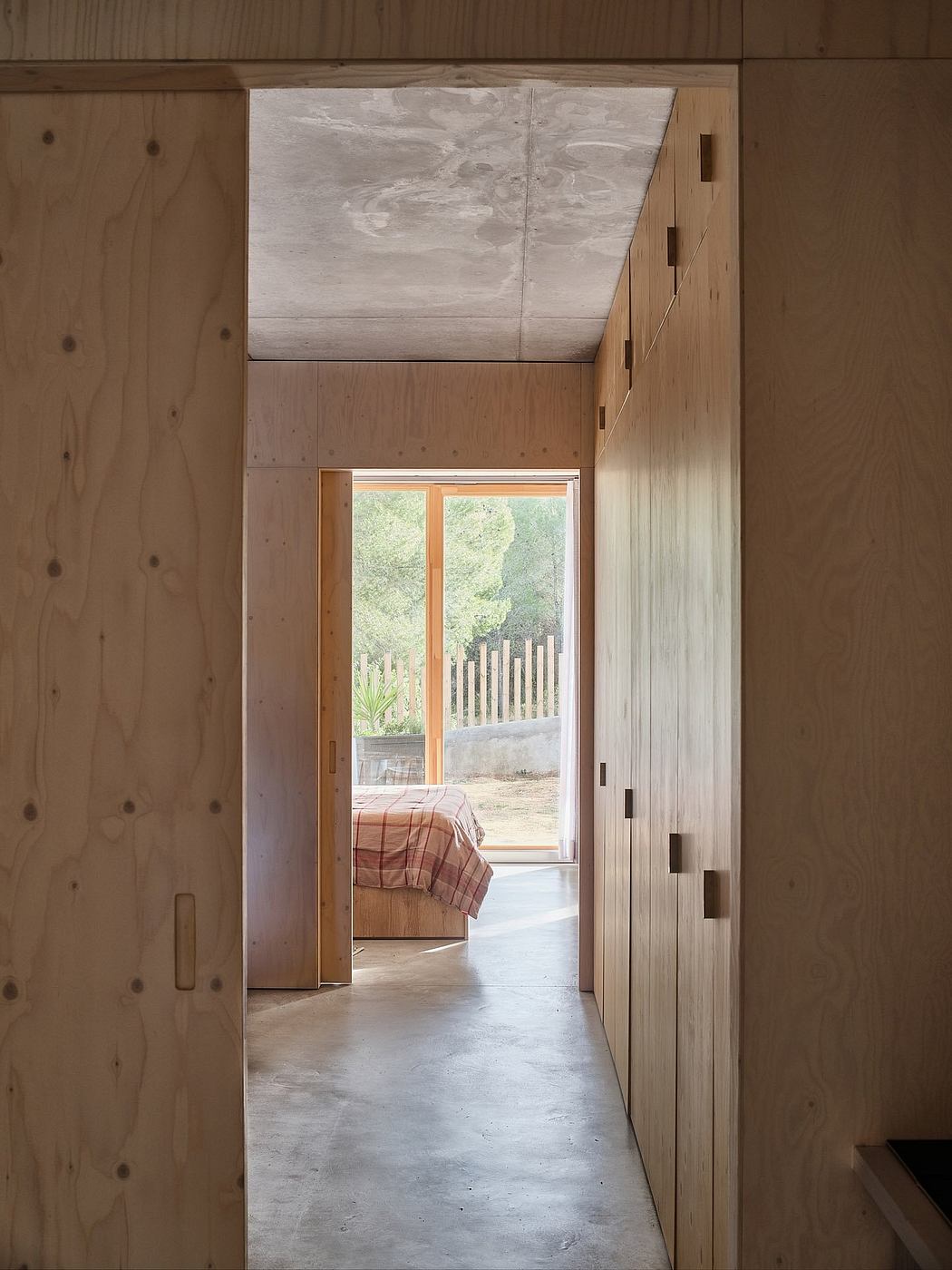 A cozy, minimalist bedroom with a wooden interior and a view of the outdoors.