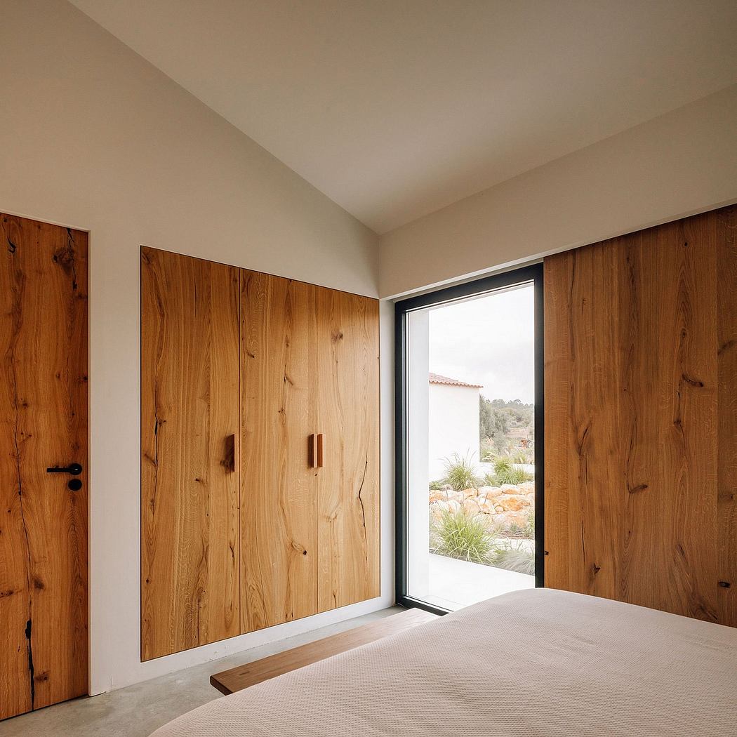 Warm, minimalist bedroom with large wooden wardrobes and a window overlooking a lush garden.
