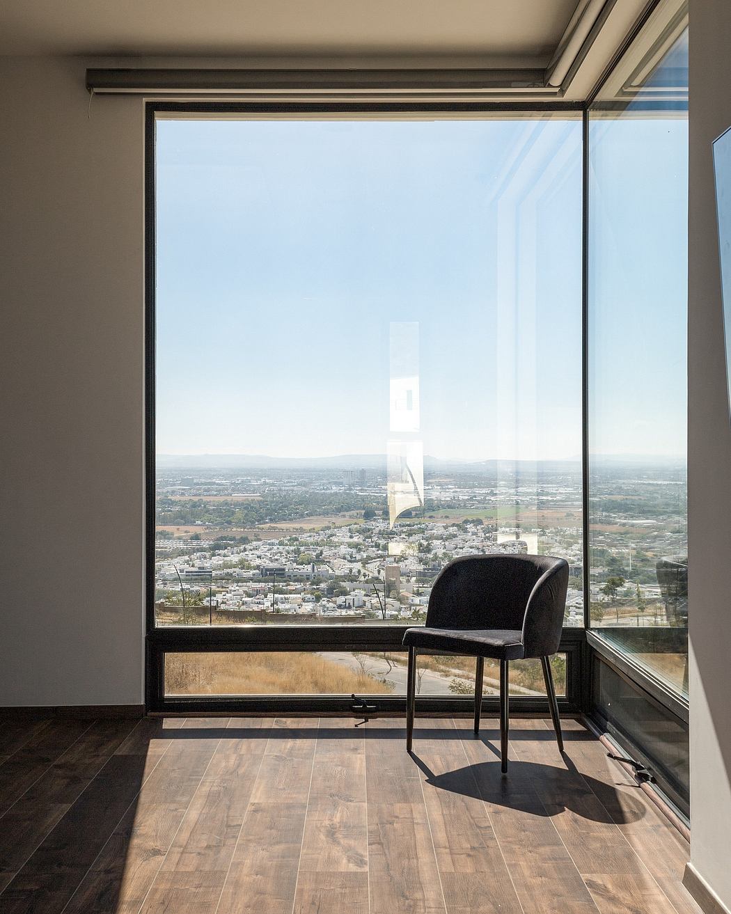 Panoramic city view through large window frames a modern, minimalist interior.