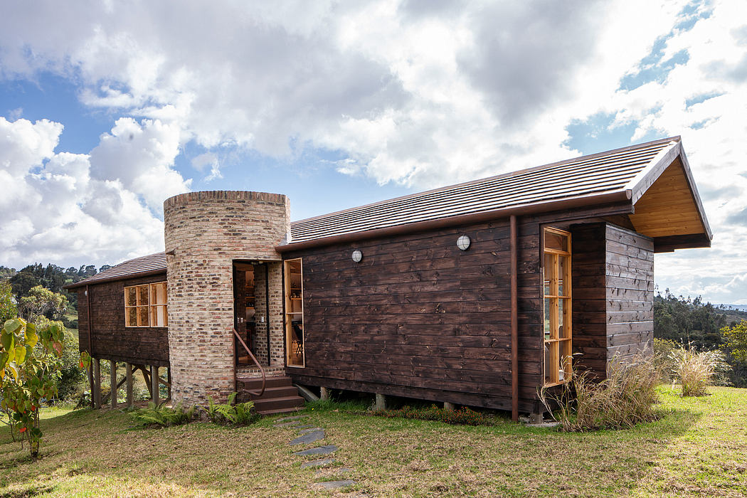 Rustic log cabin with stone chimney, raised deck, and slanted roof against cloudy sky.