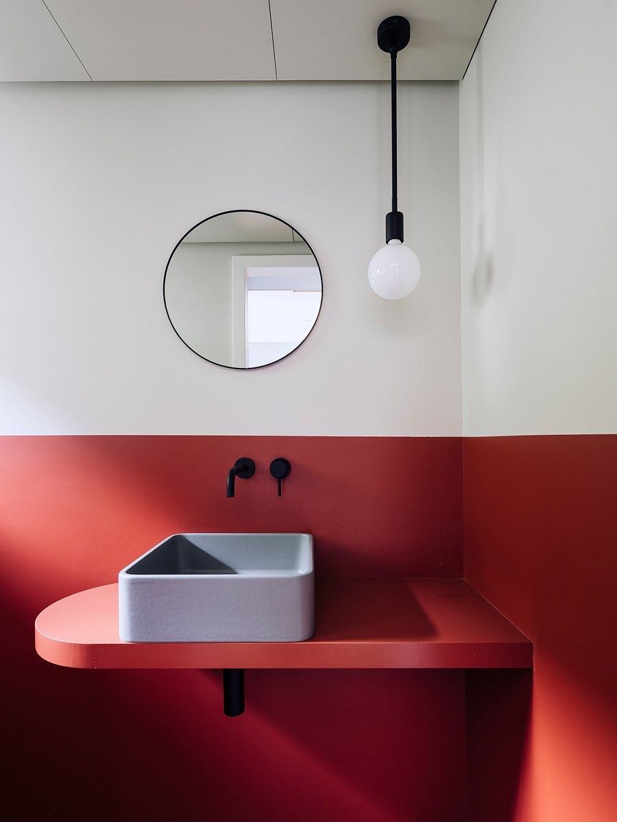 Minimalist bathroom with round mirror, black fixtures, and red accent wall.
