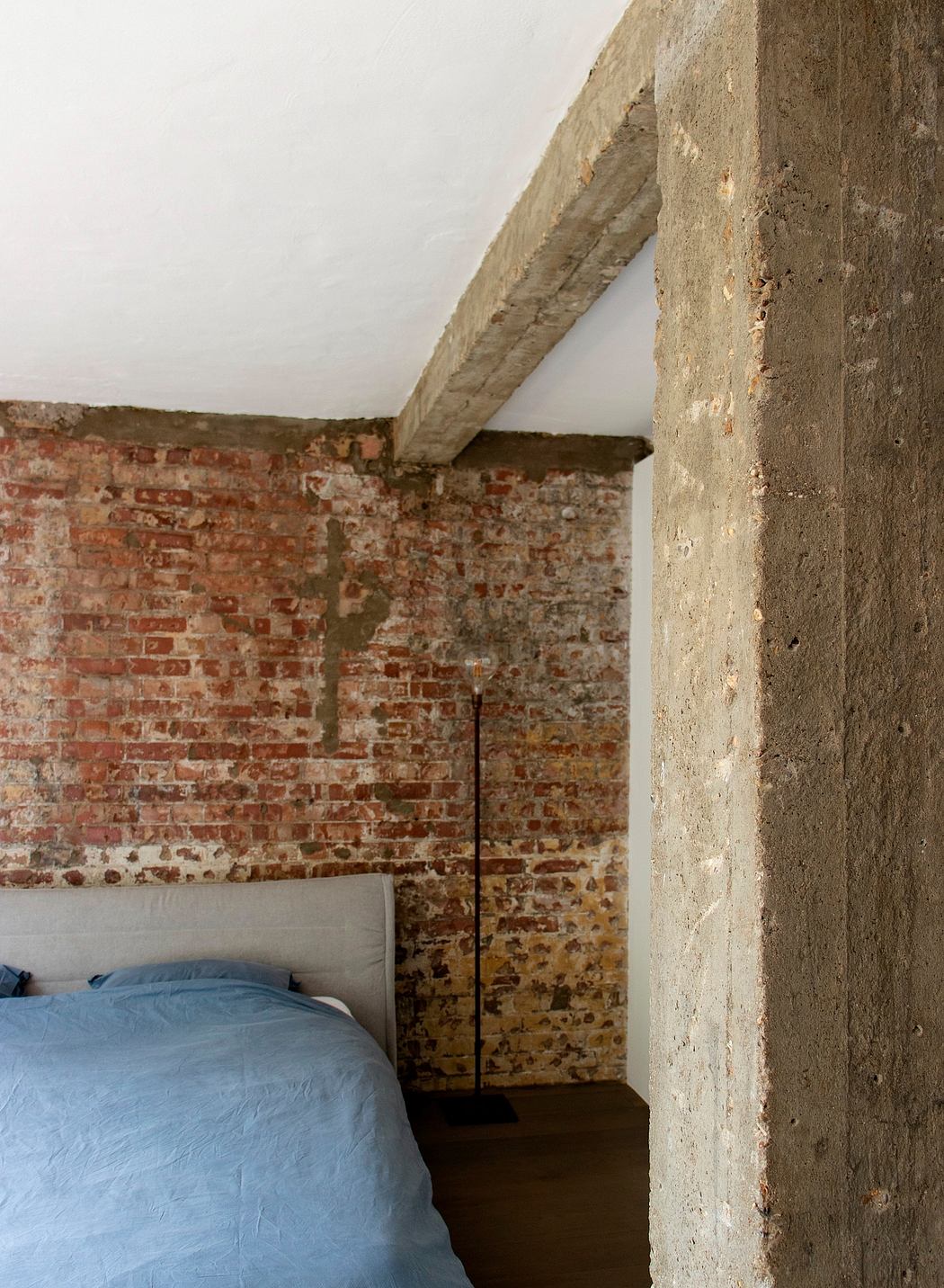 Rustic bedroom with exposed brick walls and concrete ceiling beams, creating a cozy, industrial ambiance.