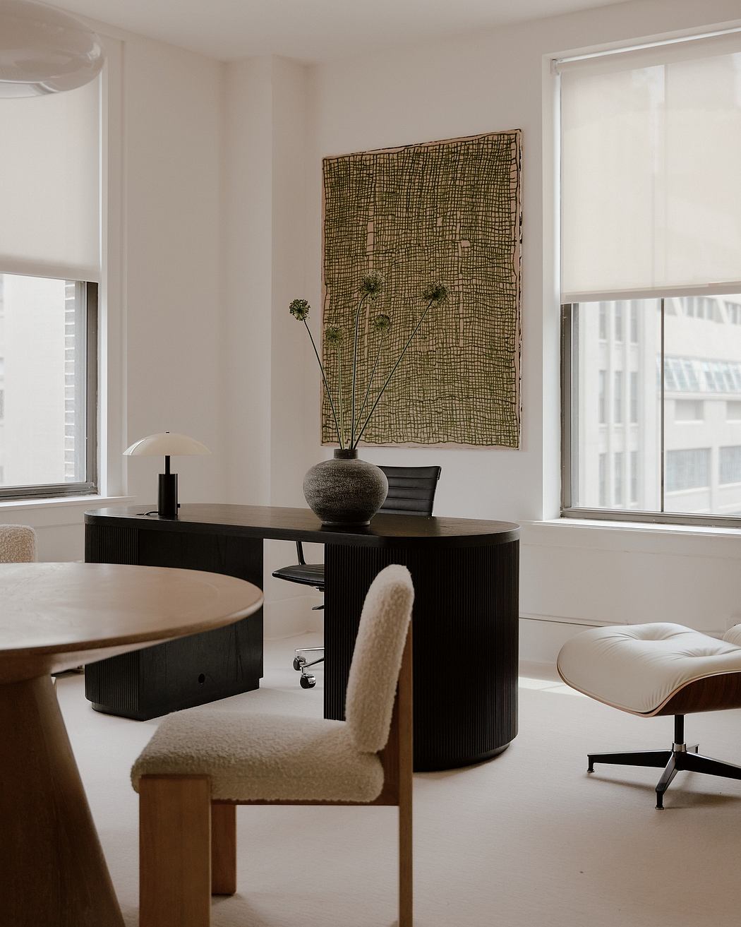 A minimalist home office with black wooden furniture, artful decor, and large windows.