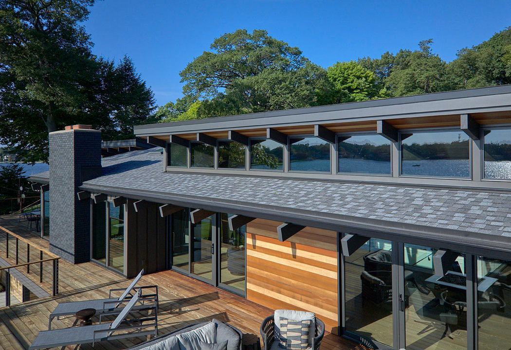 Modern lakefront home with floor-to-ceiling windows, wooden siding, and a spacious deck.