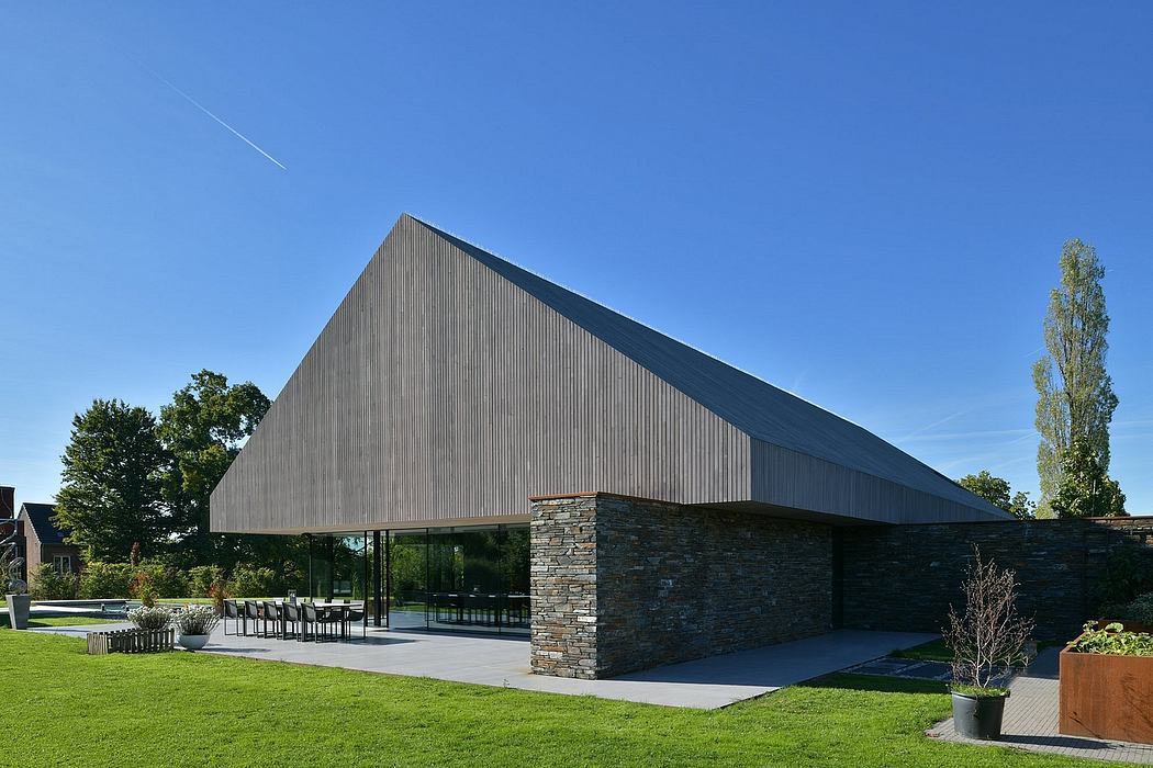 Modern, angular building with stone walls and large glass windows, set in a landscaped environment.