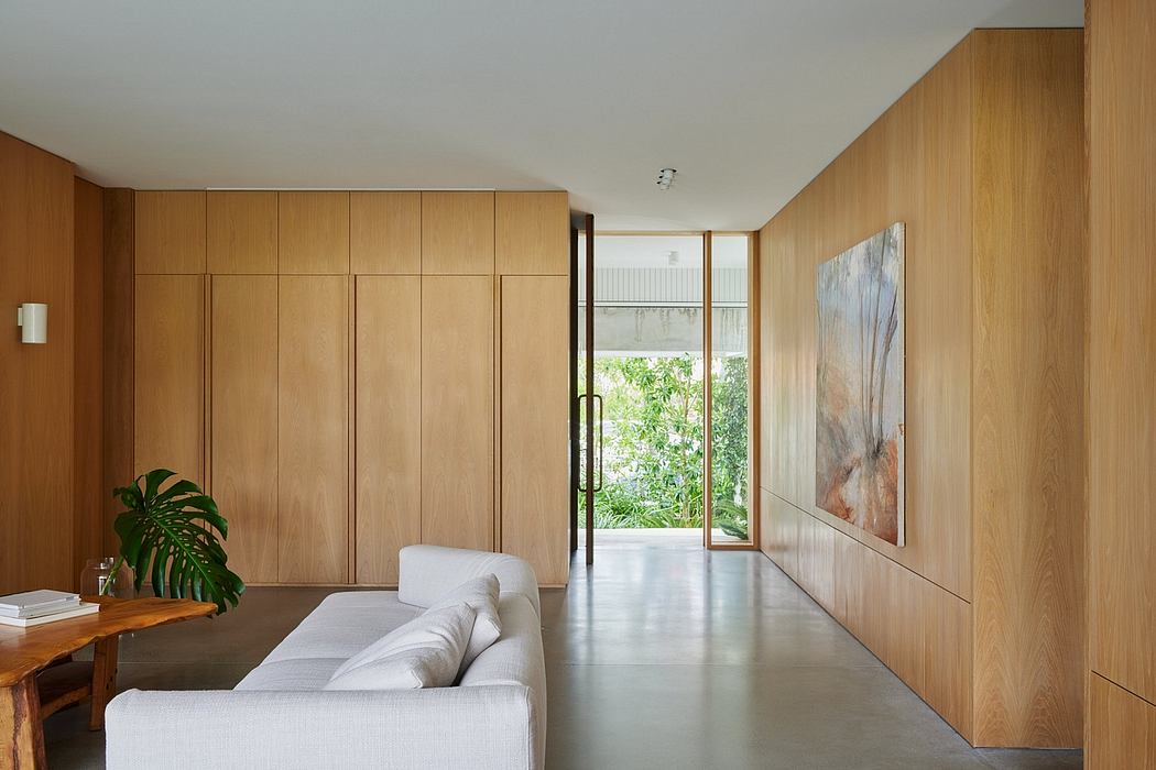 A modern, minimalist interior with warm wood paneling, concrete flooring, and a large window offering a view of greenery.