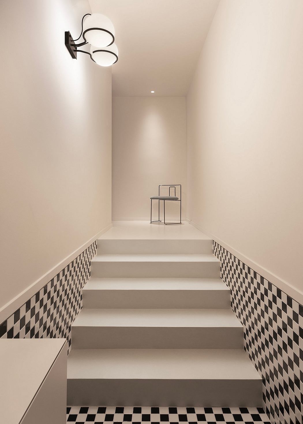 Clean, minimalist staircase with black and white checkered tiles, modern lighting fixture.