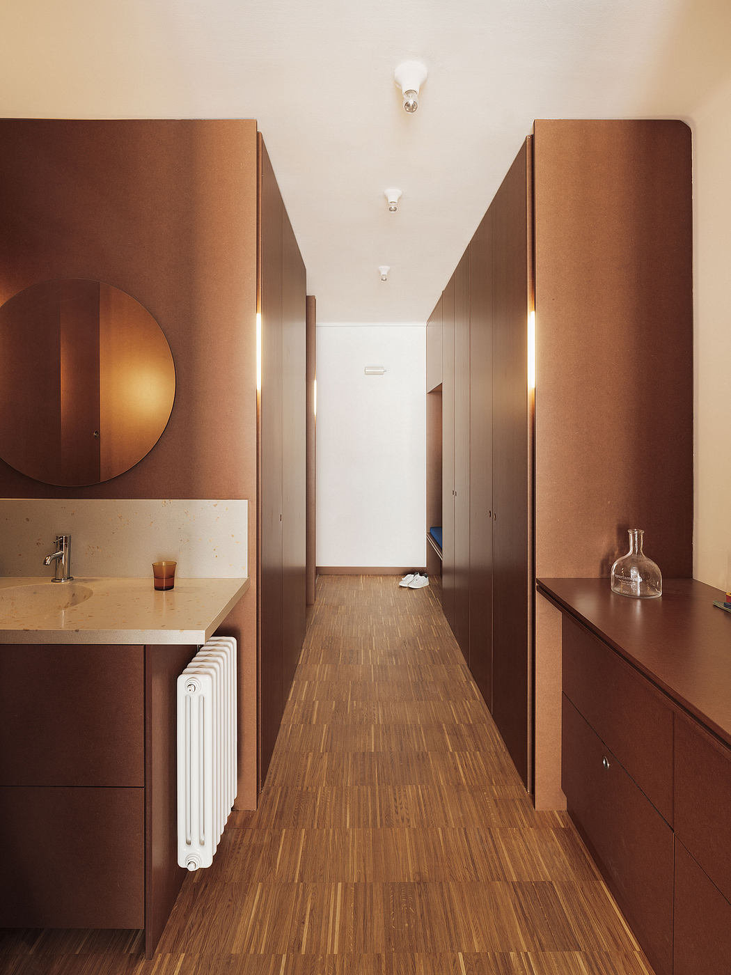 A modern, minimalist hallway with wooden floors, integrated lighting, and built-in cabinetry.