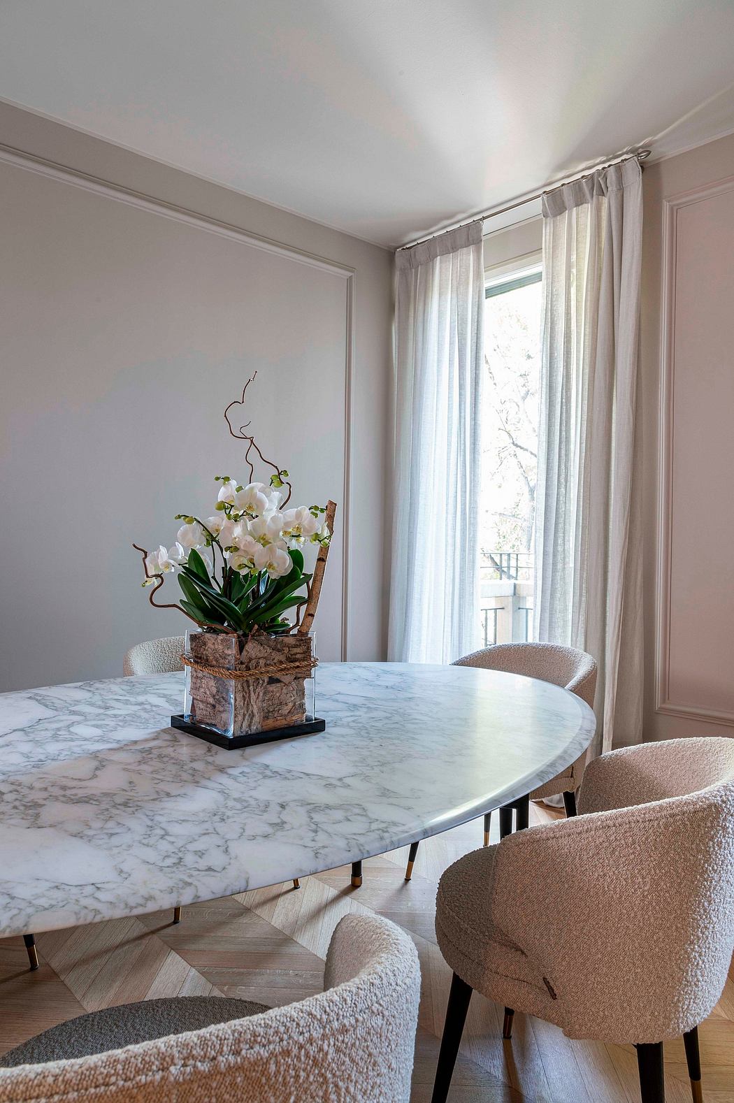 An elegant marble dining table with a striking orchid centerpiece, surrounded by plush beige chairs.
