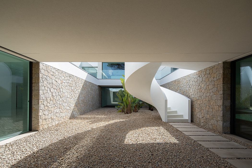 A modern architectural interior with stone walls, spiral stairs, and a gravel pathway.