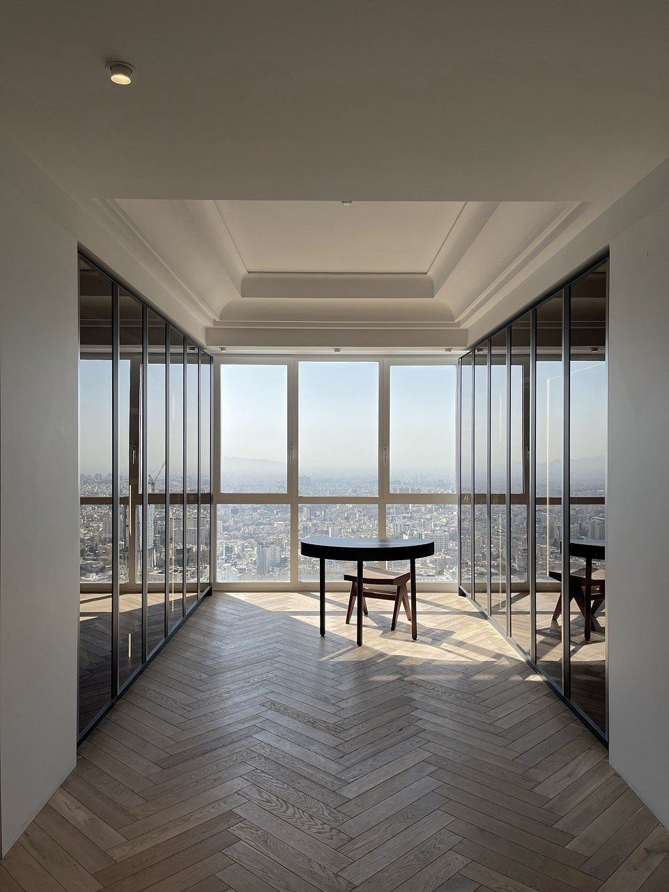 A contemporary high-rise interior with panoramic city views, herringbone flooring, and sleek furniture.