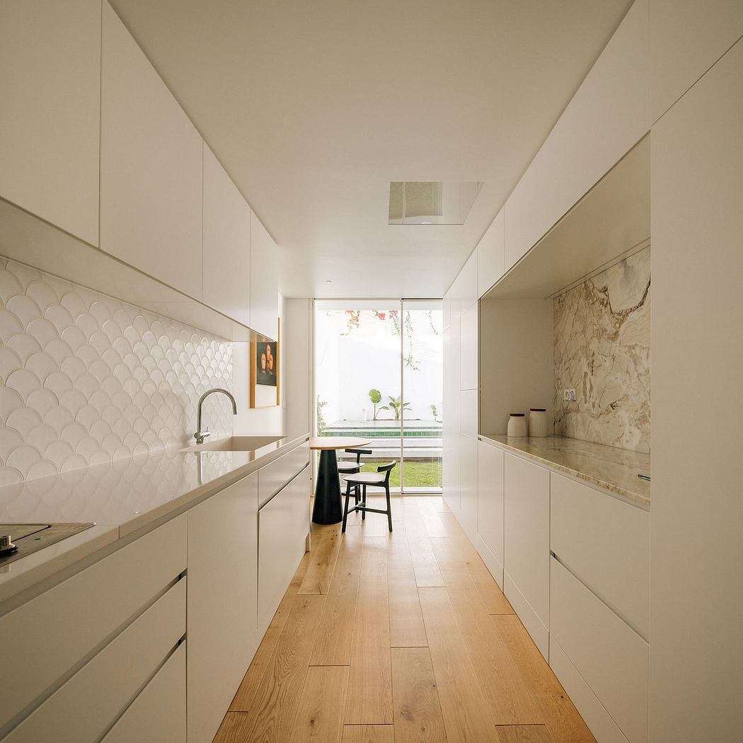 Sleek, minimalist kitchen with white cabinets, wood floors, and a view to the outdoors.