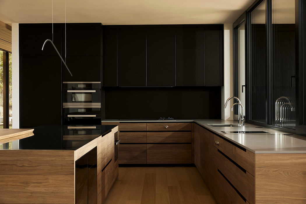 Modern kitchen with sleek black cabinetry, wood accents, and large windows providing natural light.