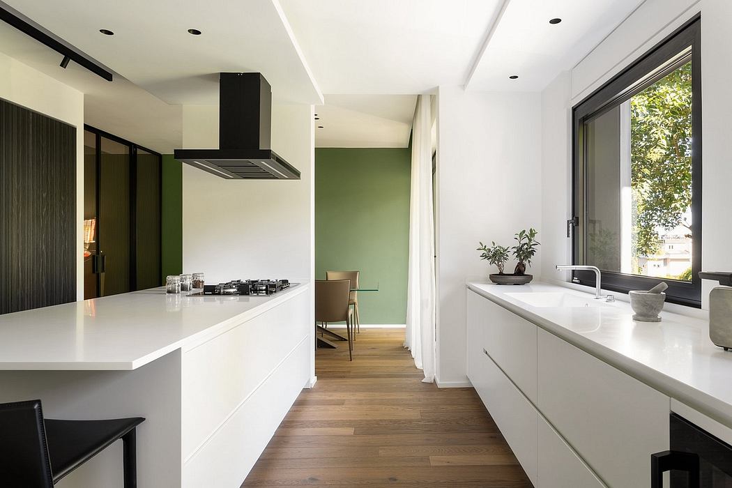 Sleek modern kitchen with white countertops, black appliances, and views to an adjacent room.