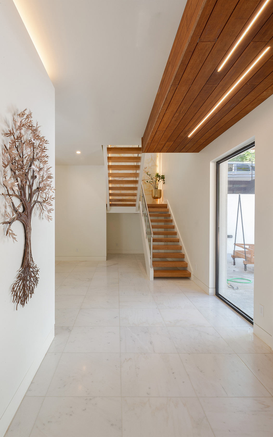 Modern open-concept entryway with wooden staircase, marble flooring, and decorative wall art.