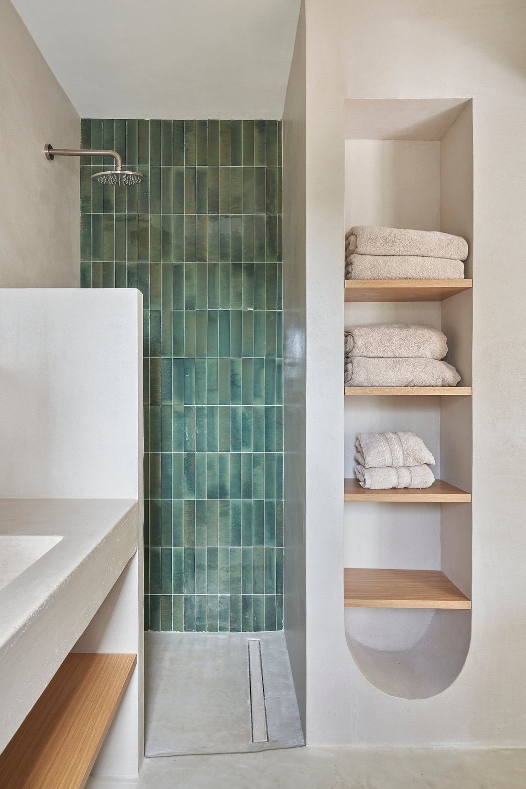 Sleek, minimalist bathroom with textured green tile wall, built-in shelving, and towels.