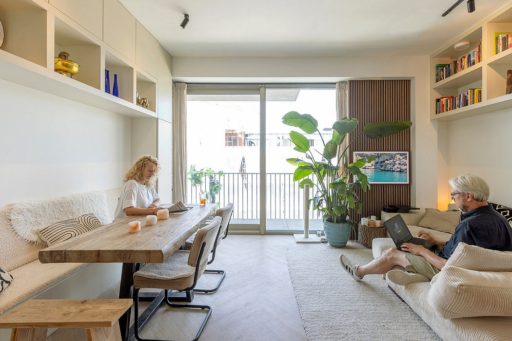 Cozy living room with large window, wooden dining table, and bookshelves lining the walls.