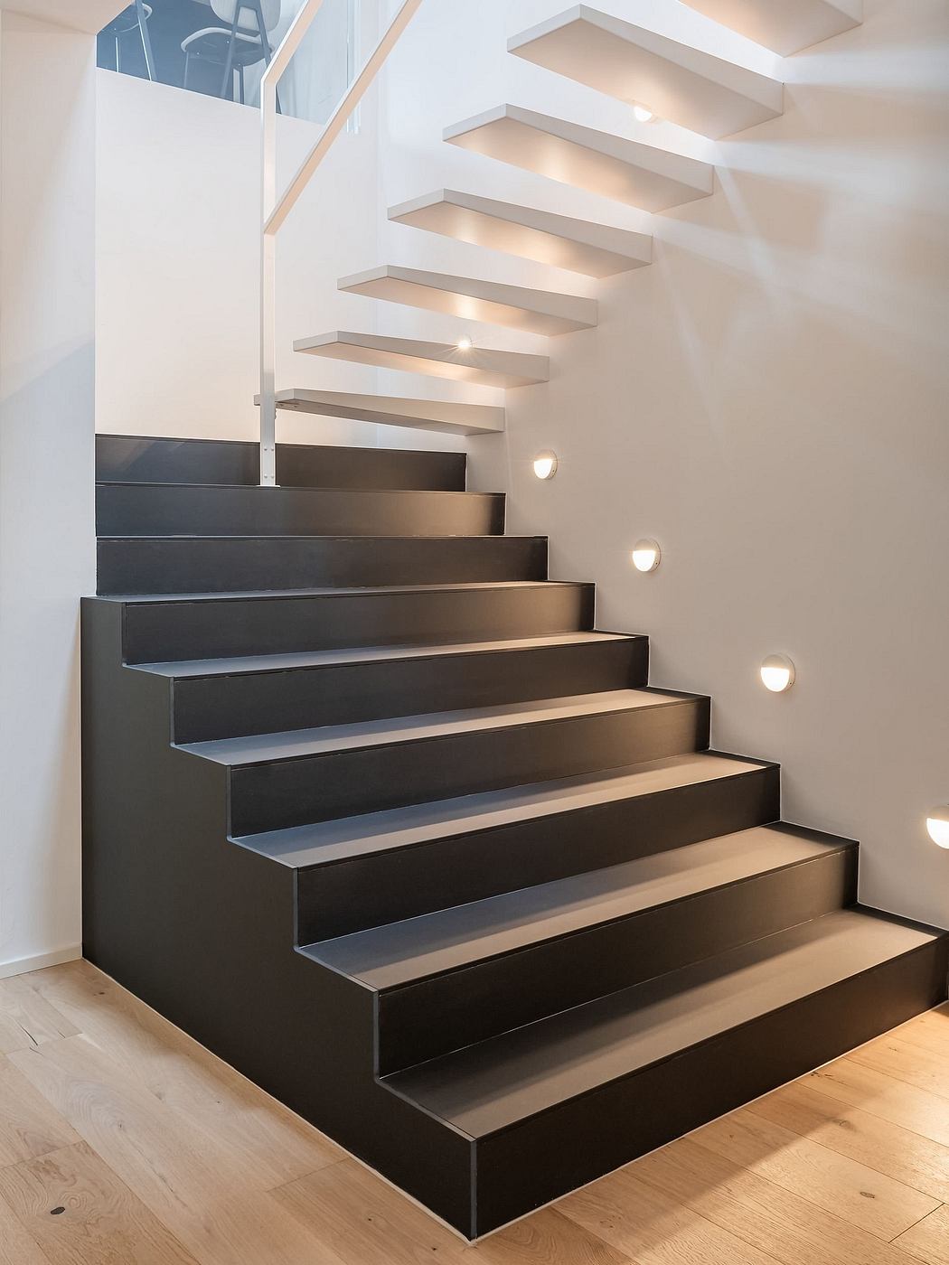 Modern staircase with floating black steps, recessed lighting, and clean lines.