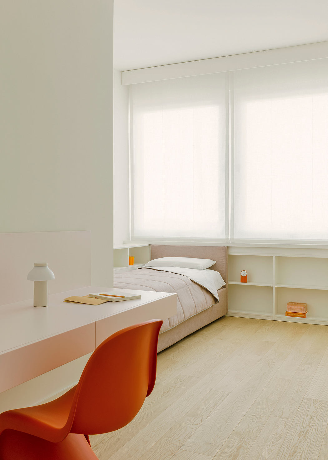 Minimalist bedroom with white walls, built-in storage, and an orange accent chair.