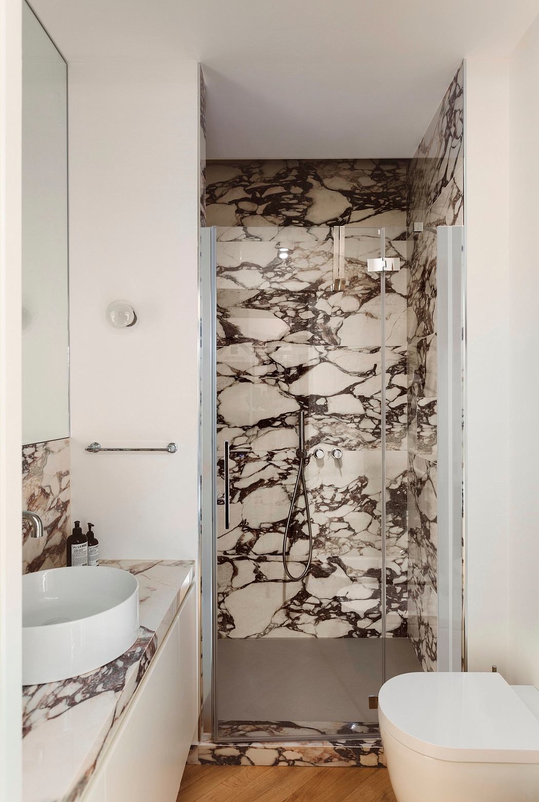 Sleek marble-clad bathroom with modern fixtures and a glass shower enclosure.
