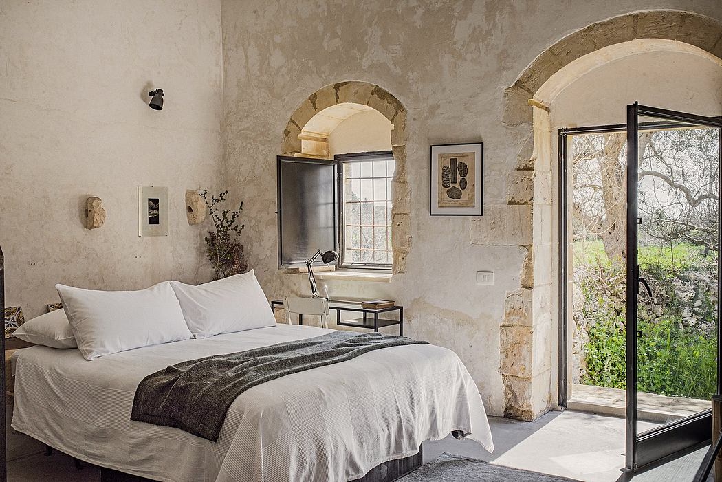 Rustic stone walls, arched windows, and minimalist furnishings in this cozy bedroom.