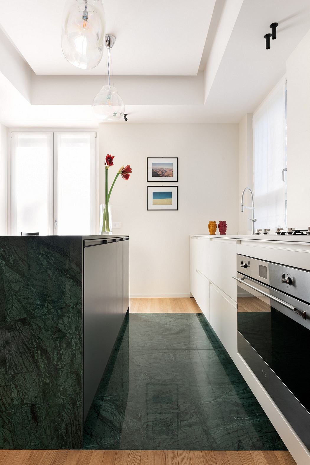 A modern kitchen with a sleek black marble countertop, white cabinetry, and minimalist lighting.