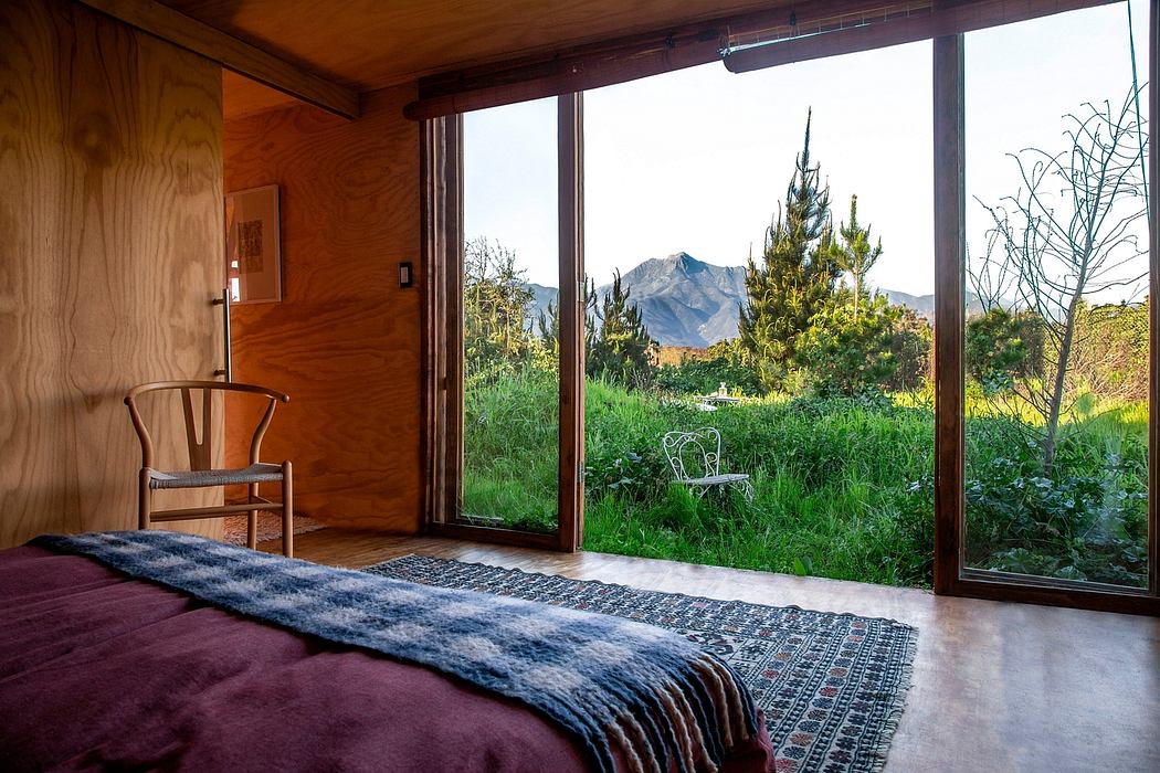 A cozy bedroom with a wooden interior, large windows, and a scenic mountain view.