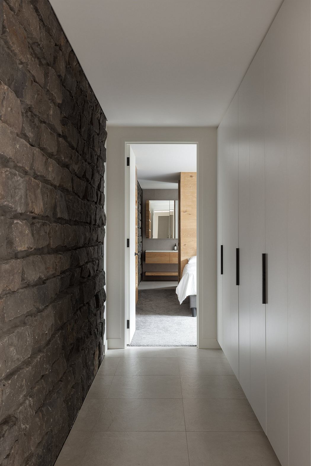 Minimalist hallway with stone wall, wooden elements, and sleek white doors leading to bedroom.