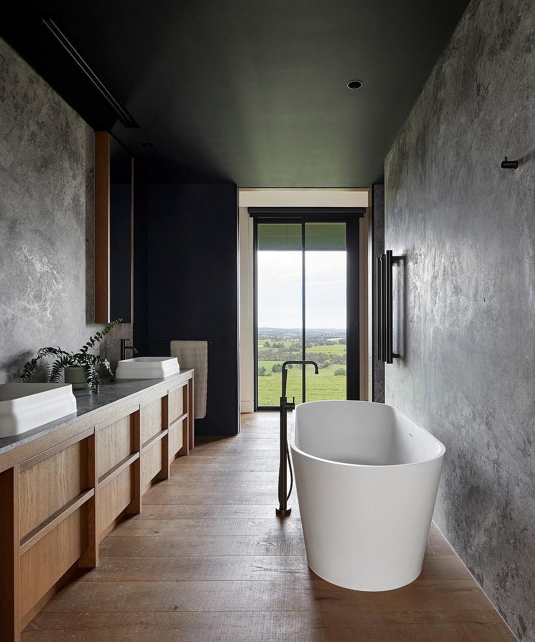 A minimalist bathroom with a freestanding tub, wooden vanity, and panoramic countryside view.