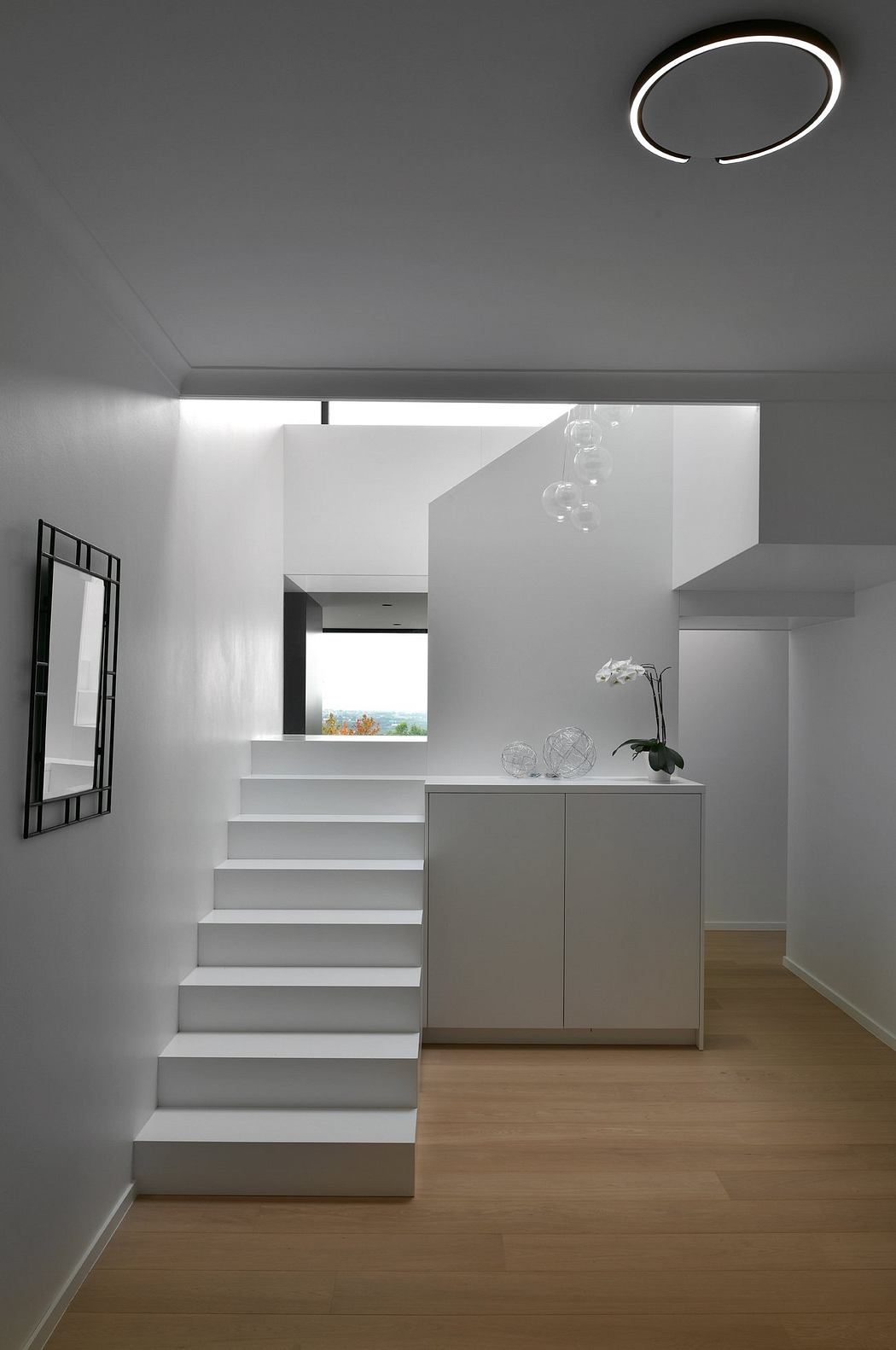 A modern, minimalist interior with clean lines, a floating staircase, and a sleek cabinet.